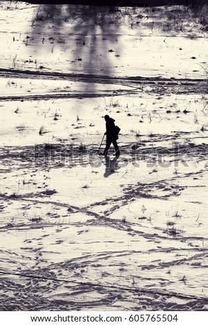 Silhouette of pedestrian with stick. Man walks along trail in snow. Winter landscape with city street. Toned black and white photo