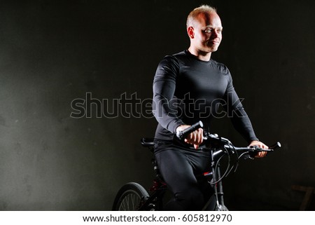 cycle man with bike indoors. Man in black cycling Apparel on gray wall background.