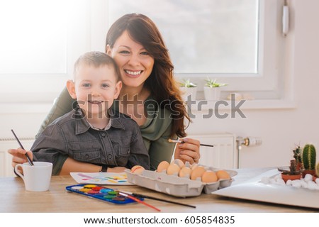Mother and son painting Easter eggs with smile