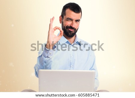 Man with laptop making OK sign on ocher background