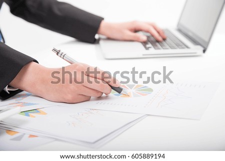 Side view and close up of woman's hands using laptop and writing on business document
