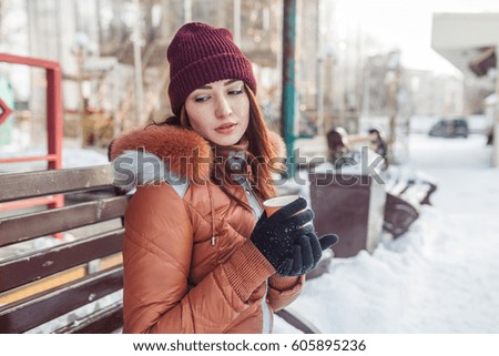 The girl walks in fine winter day. She sits on a bench and has the invigorating, warm coffee. She looks somewhere in a bottom as if she thought of something. The girl has very beautiful look.