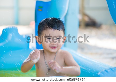 Asian kid playing in inflatable baby pool. Boy swim and splash in colorful swimming pool with water toys on hot summer day.