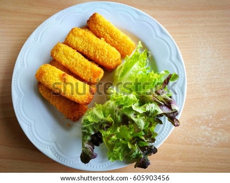 Top view of crispy fish fingers sticks and red green oak vegetables on a white plate (put on old wooden table); copy space on the right