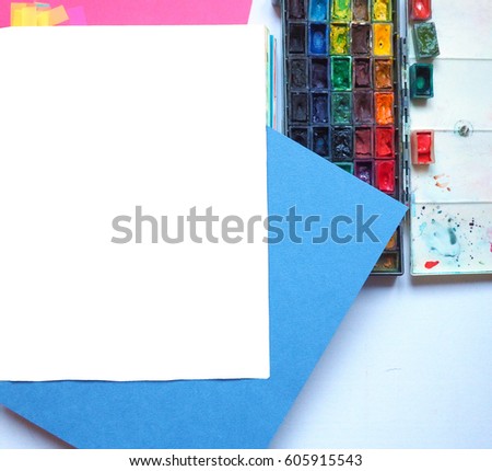 Art table colorful sheets of paper and blank notebook with drawing tools on yellow background. Top view with copy space
