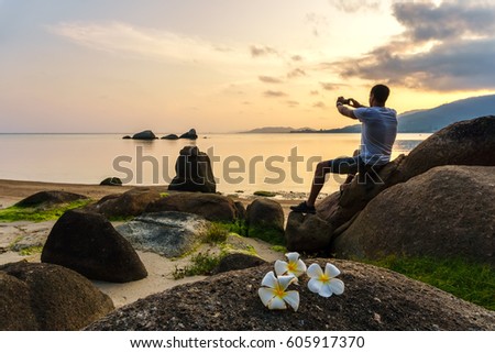 Man sits on the beach and takes a picture of the sunset by phone