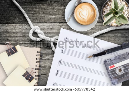 Sheet music, cactus, fountain pen, tape cassette and coffee latte on vintage wooden table