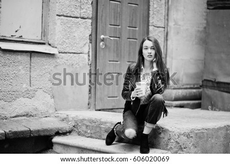 Portrait of stylish young girl wear on leather jacket and ripped jeans with cup of coffee. Street fashion model style. Black and white photo.