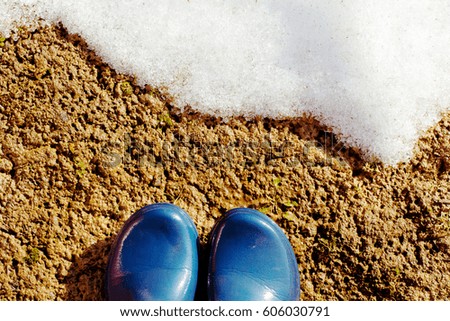 Blue rubber boots on the wet ground  in front of the melting snow. Sunny day.