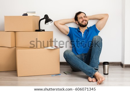 young happy man lying on the floor in his new apartment with packing boxes near him