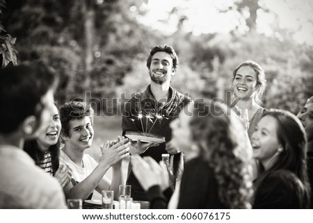 A group of young people gathered on a terrace to celebrate the birthday of one of their friends. A young man holding a cake with candles on it. Black and white picture