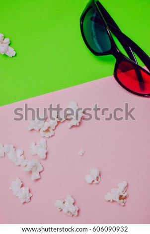 Popcorn and 3D glasses on green and pink background.