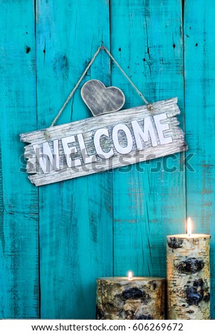 Wood welcome sign with heart and burning log candles hanging on antique teal blue weathered wooden background; holiday, Valentines Day and Mothers Day background with rustic decor