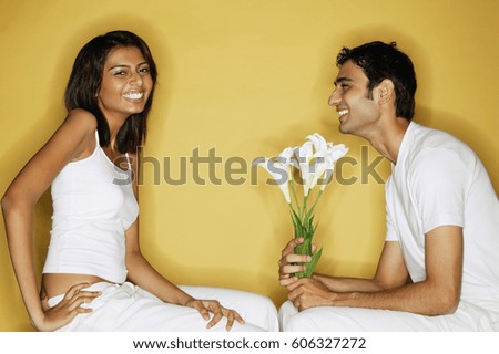 Couple sitting face to face, woman looking at camera, man holding bouquet of flowers