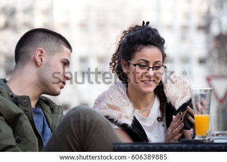 Two friends boy and girl sitting in coffee shop and having fun looking at smartphone