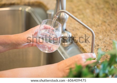 Woman Pouring Fresh Reverse Osmosis Purified Water Into Glass in Kitchen. Royalty-Free Stock Photo #606409475