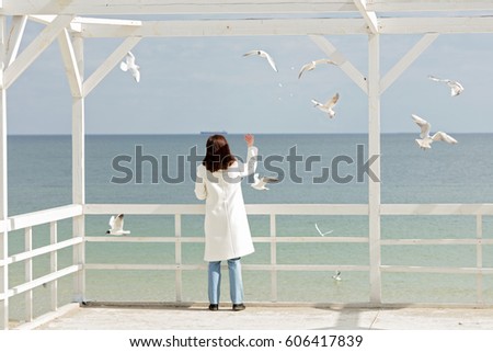 Young woman (brunette) in a white coat feeds the gulls on the beach. Selective focus.