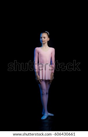 young ballerina girl dancer shows dance elements on a black background in a blue stage light