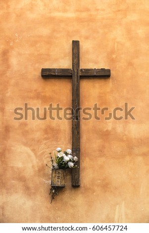 Old wooden christian cross on a wall decorated with flowers on the street in Rome, Italy