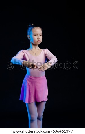 a young girl aspiring dancer shows dance elements on a black background in a blue stage light