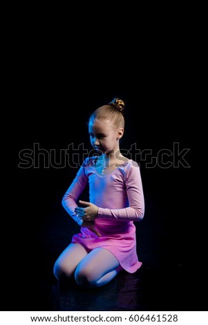 a young girl aspiring dancer shows dance elements on a black background in a blue stage light