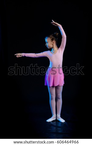 a young girl aspiring ballerina dancer shows dance elements on a black background in a blue stage light