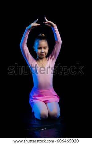 a young girl aspiring ballerina dancer shows dance elements on a black background in a blue stage light