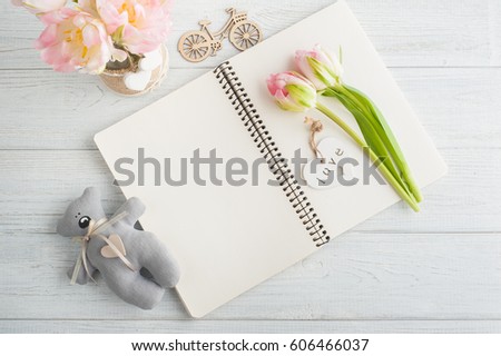 Overhead shot a bouquet of pink tulips and teddy bear over white wood table top with an open journal. Flat lay top view style.