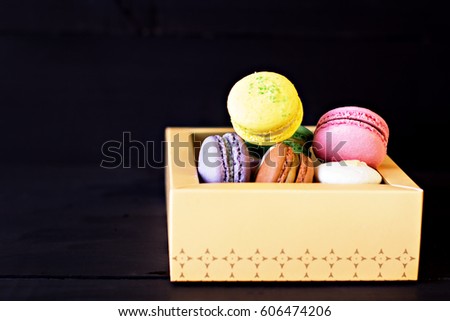 Multicolored macaroons in a box on a black background.