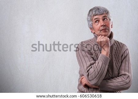 A portrait of thoughtful dreamy senior man standing over white background with copy space for your advertisement.  Mature man deep in thought trying to remember something from his life