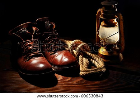 Still life of travel boots, old latern kerosenelamp and sailor rope on wooden background