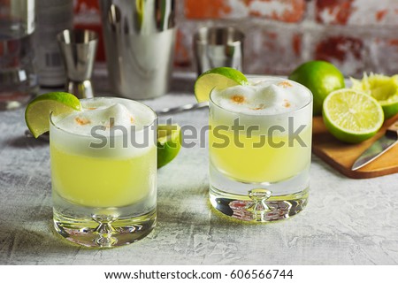 Two Pisco Sour Cocktails with Ingredients and Bottles on a Bar Royalty-Free Stock Photo #606566744