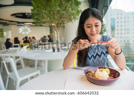 Young asian chinese girl sitting in the restaurant and taking pictures of the food with mobile smartphone. People having fun by restaurant in the food court on travel in Thailand, Asia.