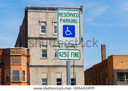 The "Reserved Parking for Disabled" sign with buildings and blue skies in the background.