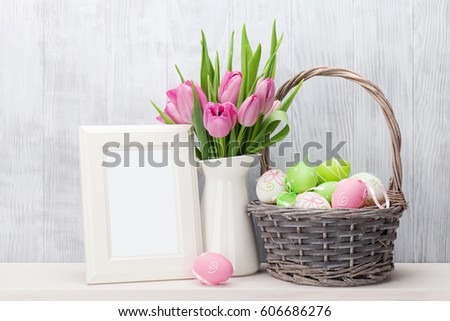 Easter eggs, blank photo frame and pink tulips bouquet on shelf in front of wooden wall. View with copy space