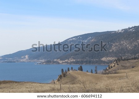 Mountains, meadow and lake landscape in springtime with house on edge of hill above lake.
