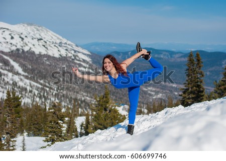 The girl in the blue outfit doing yoga on top of a mountain in winter
