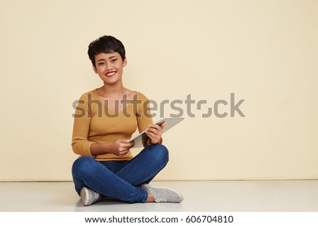 Joyful Filipino woman with tablet sitting on the floor with digital tablet