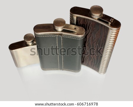 Three flat flask for alcohol on a glass table isolated on a gray background