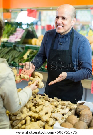 Mature seller offering female fresh roots of ginger in grocery
