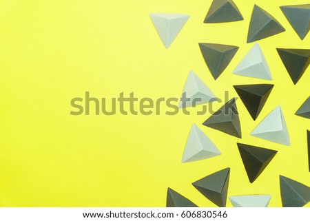 Grey and black origami tetrahedrons on yellow background with copy space on the left side.