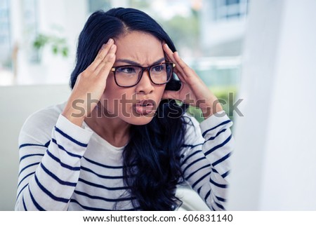 Frowning Asian woman looking at laptop with hands on head in office