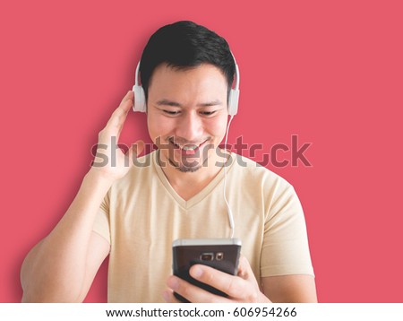 Asian man is relaxing by listening to happy music in his smartphone isolated on pink background.
