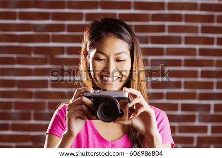 Smiling asian woman taking picture with camera on brick wall