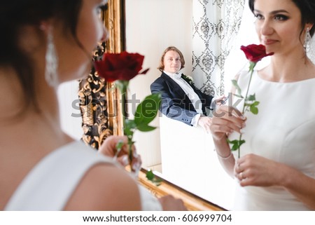 Groom admires bride while she looks at herself in the mirror