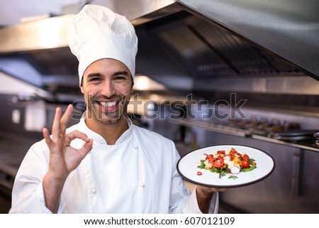 Handsome chef showing ok sign and meal in a commercial kitchen