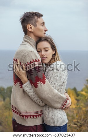 Happy thoughtful couple standing on a cliff near sea hugging each other in cold foggy cloudy autumn weather. Copy space