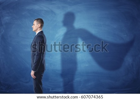 Businessman is standing in profile casting a shadow of the superman's cape on blue chalkboard background. Inner strength. Leader's qualities. Ready for profit and development