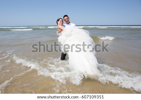 The groom carries his bride in his arms feet in the water of the sea