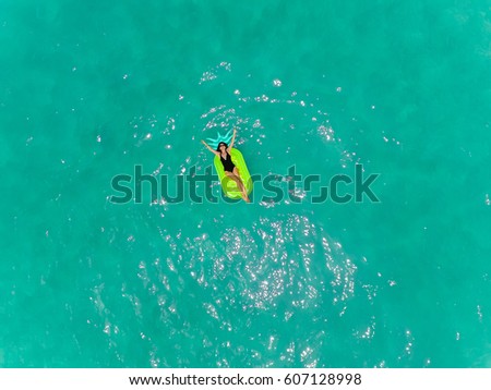 Aerial view of brunette woman swimming on the inflatable big pineapple in the transparent turquoise sea. Top view of slim lady relaxing on the floating mattress. Thailand, Phuket, Andaman sea.